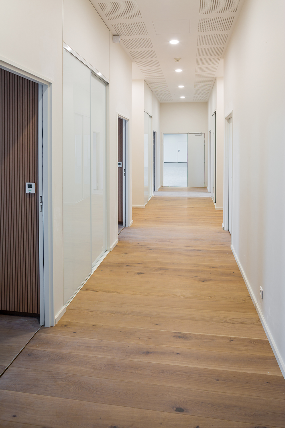 Un couloir avec un parquet en bois qui dessert différents bureaux