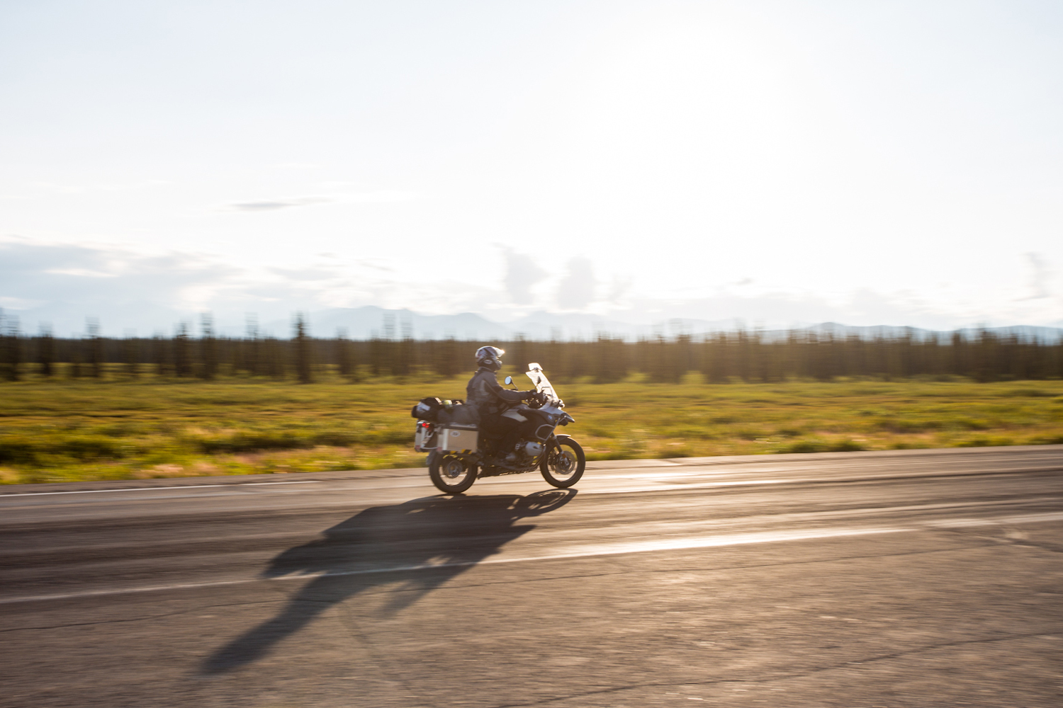 Une moto roule sur une route en Alaska au soleil couchant
