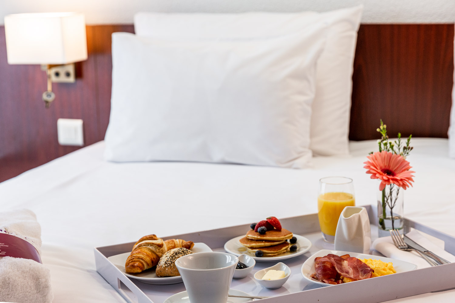 Photographie d'un plateau avec un petit déjeuner complet dessus. Le plateau est sur le lit de la chambre d'hôtel.