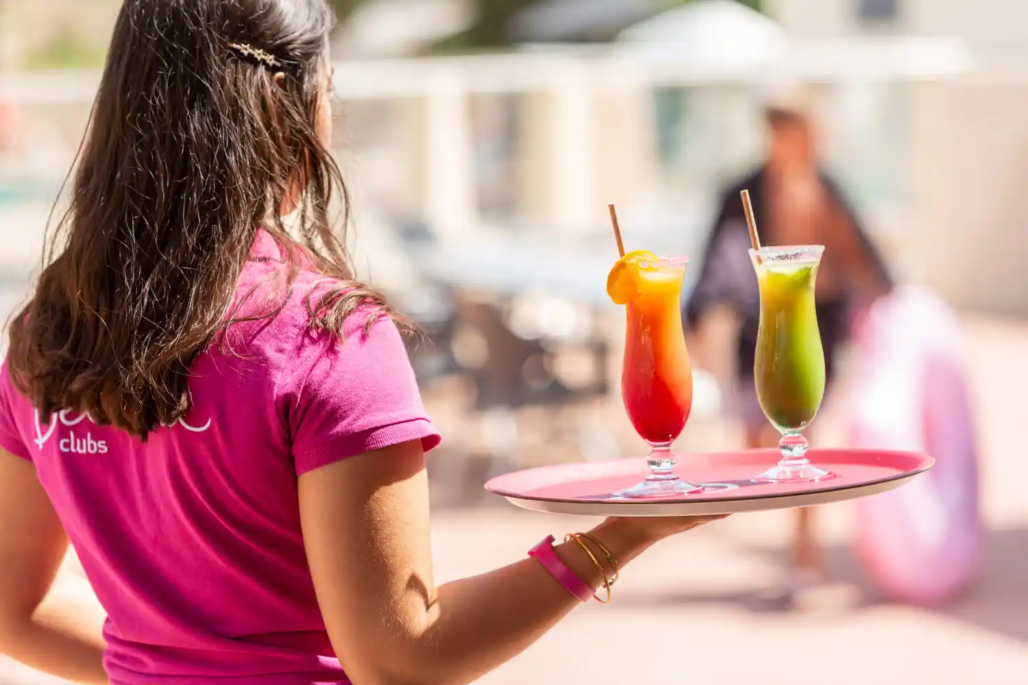 Une serveuse s'avance avec un plateau et deux verres à cocktail dans un bar. Photographie de mise en situation pour un hôtel